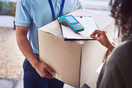 Closeup shot of an unrecognisable woman using a credit card to pay for her delivery from the courier